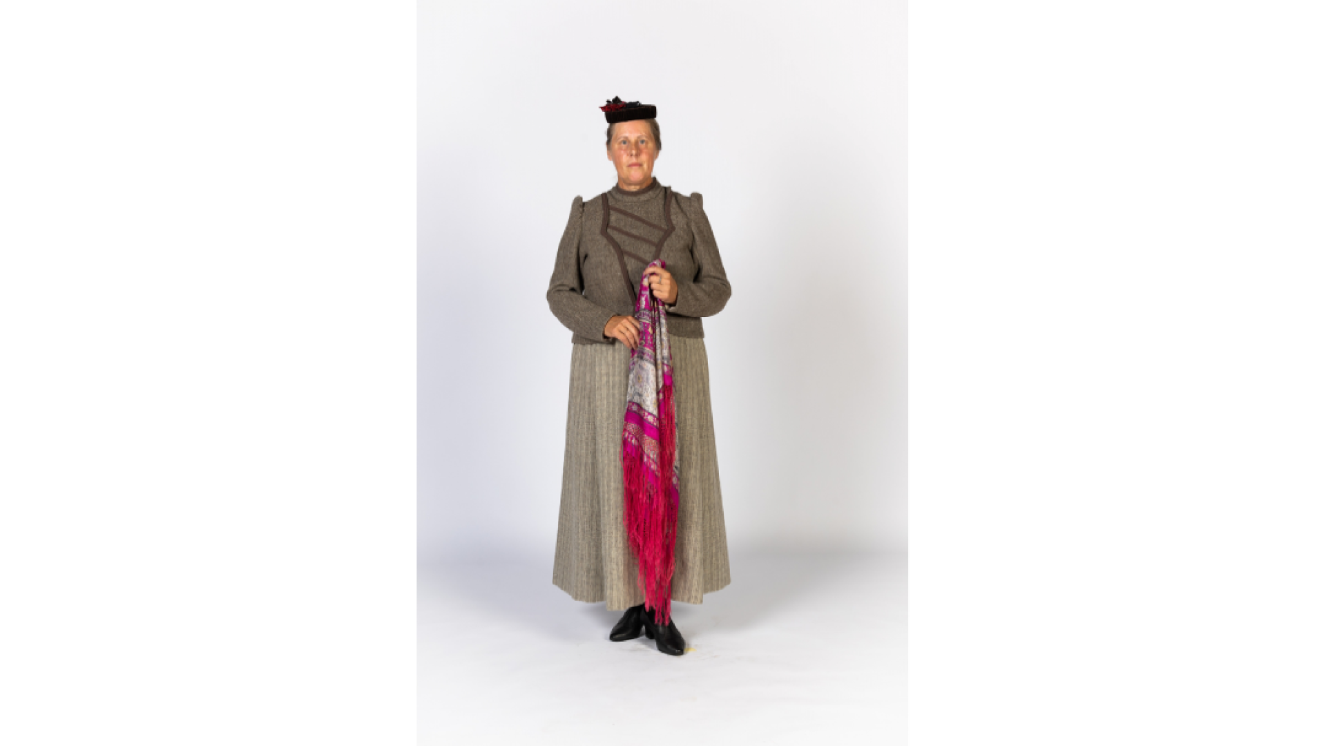 Sieviete 19.gs beigu pilsētas tipa apģērbā. Kostīms brūnganos toņos, šūts no pašausta auduma. Galvā neliela cepurīte, rokās puķains lakats.