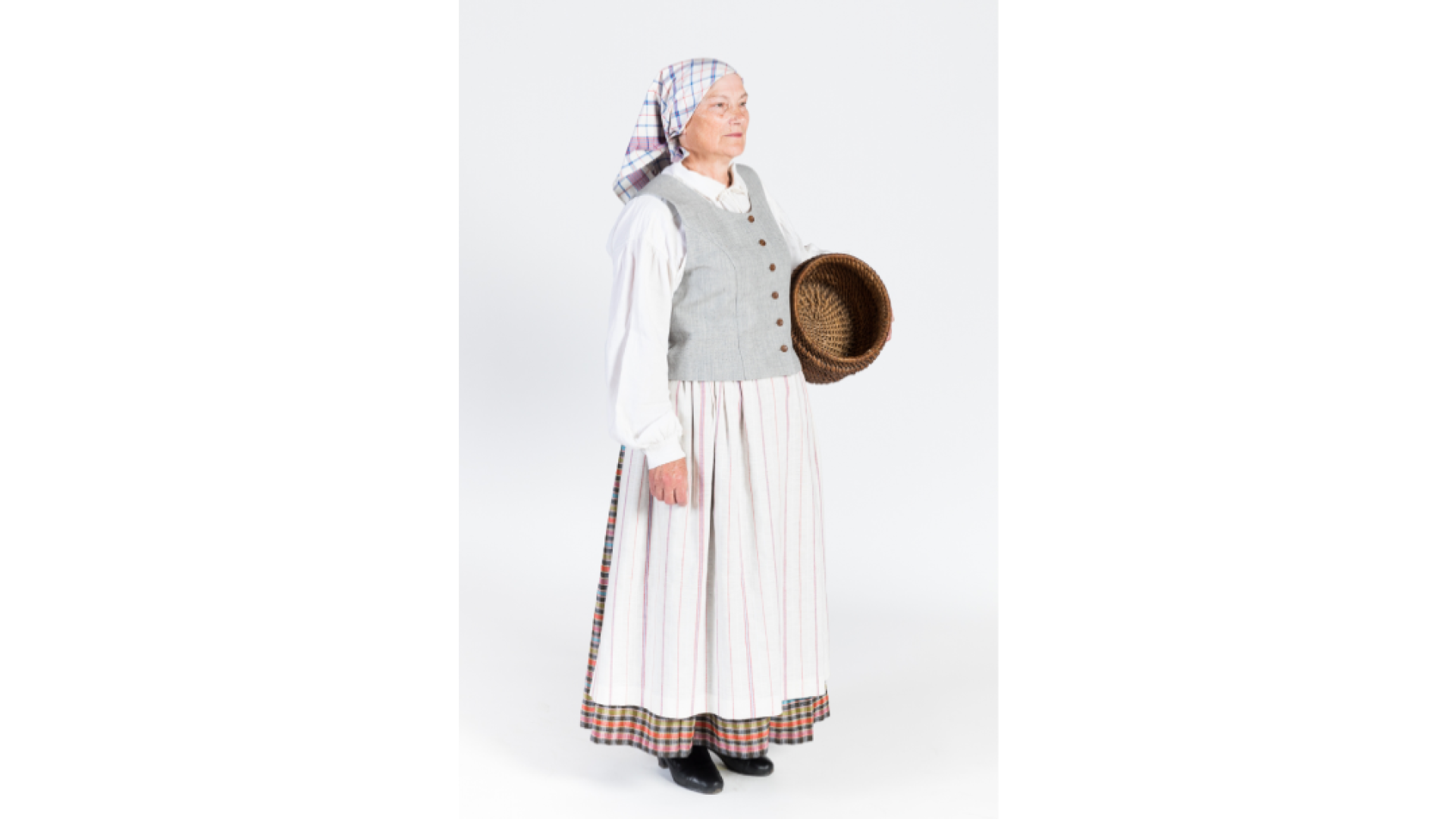 Sieva lina un kokvilnas auduma darba tērpā. Balts krekls, rūtaina auduma brunči, pelēka auduma ņieburs, priekšauts, zeļes, apavi, galvā rūtains lakatiņš.