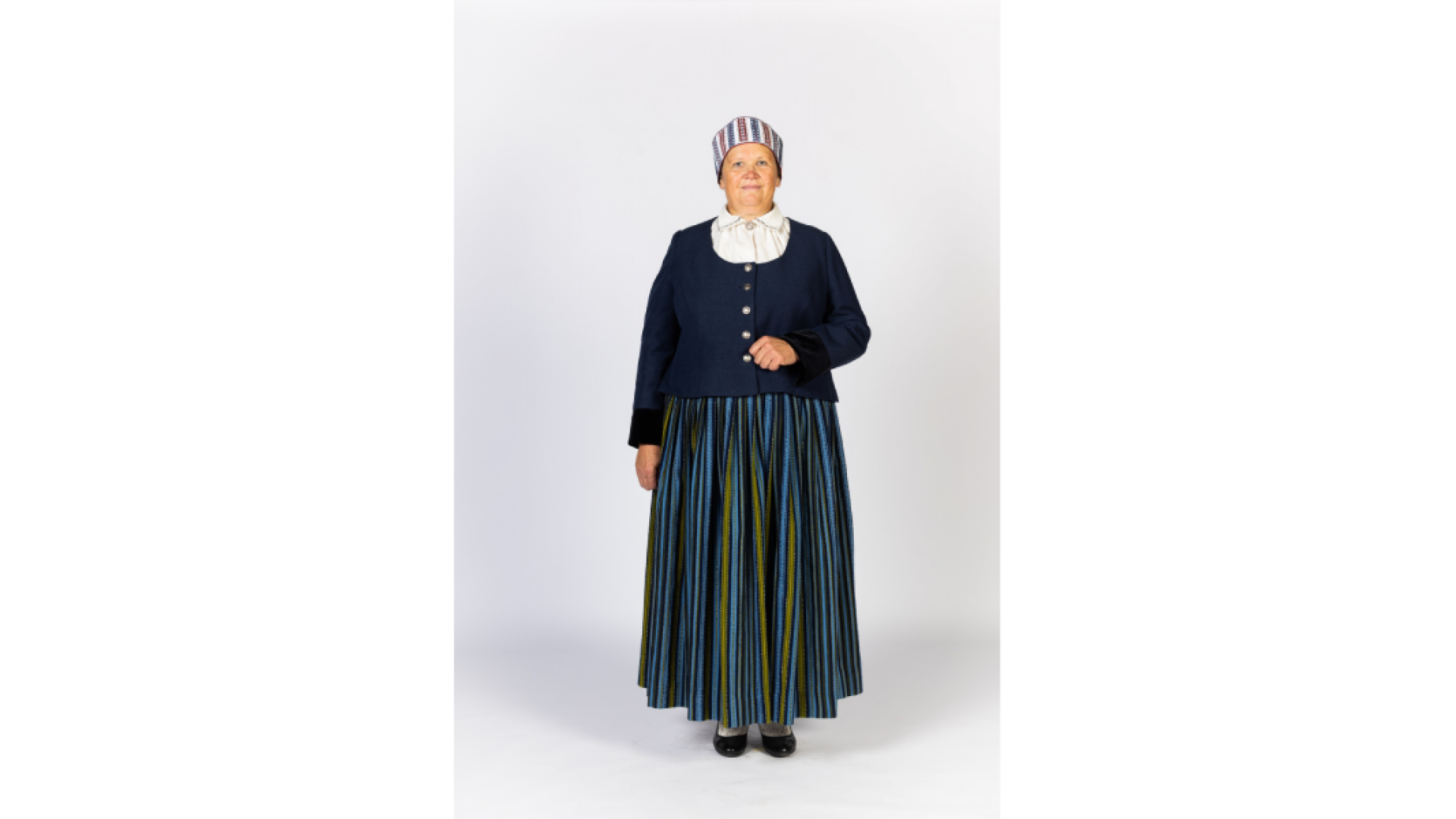 Vidzemes vidienas sievas tērps. Strīpaini brunči, tumši zila jaka, izšūta sievas vainagcepure, adītas zeķes, melnas kurpes.