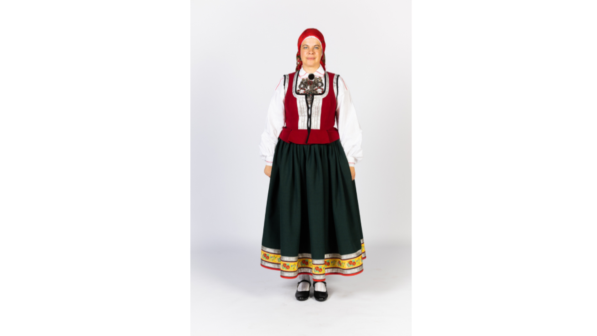 Sieviete Virgas tautastērpā. Mugurā melna auduma brunči, kuri lejasmalā rotāti ar dekoratīvām lentām, sarkans ņieburs, galvā lakats, kurš sasiets uz aizmuguri.