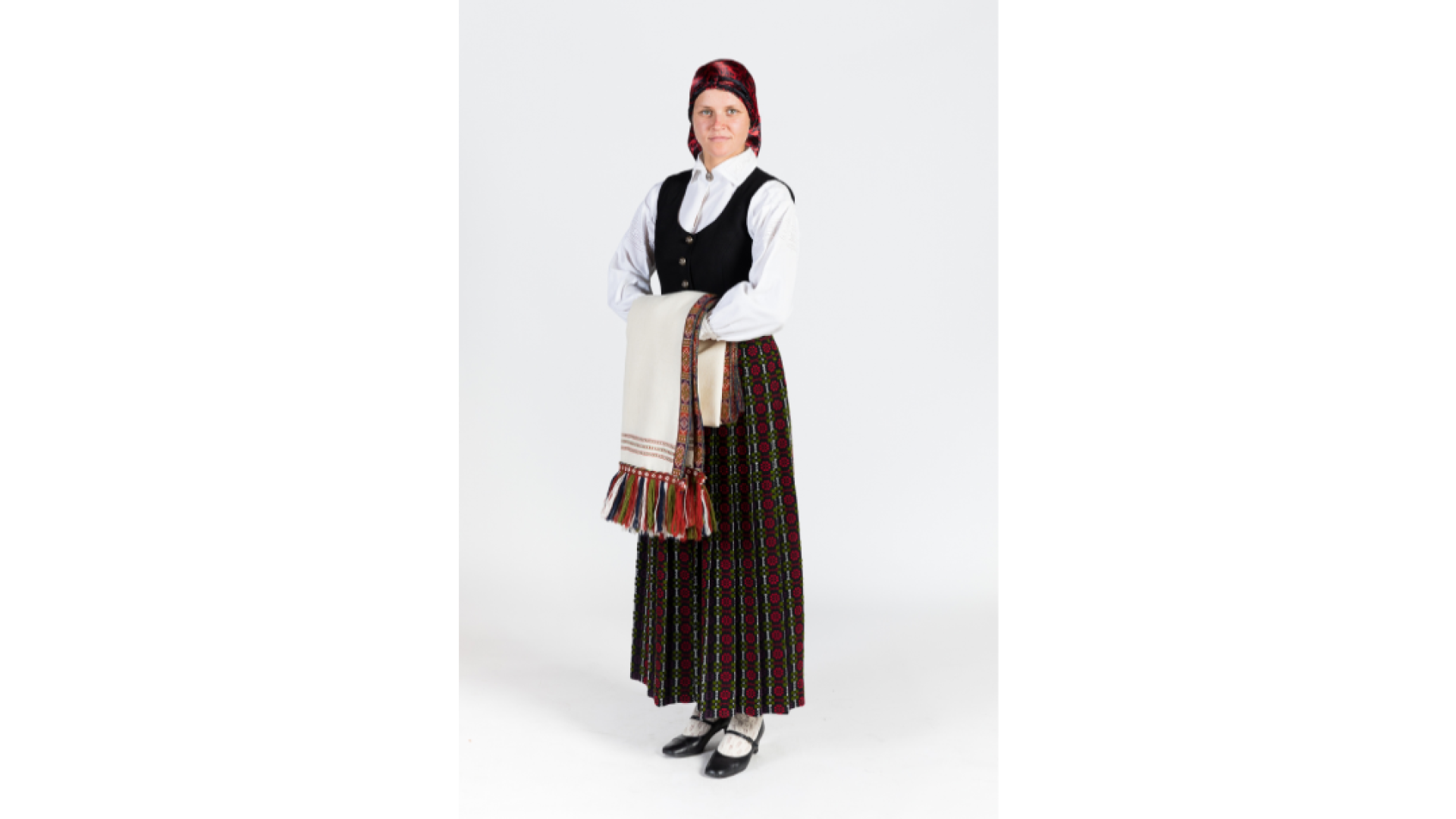 Jauna sieviete Zemgales tērpā. Tumši rozīšu brunči, tumša auduma ņieburs, krekls, galvā zida lakats, baltas, adītas zeķes, kurpes. Uz rokas tur Zemgales villaini ar apaudiem.