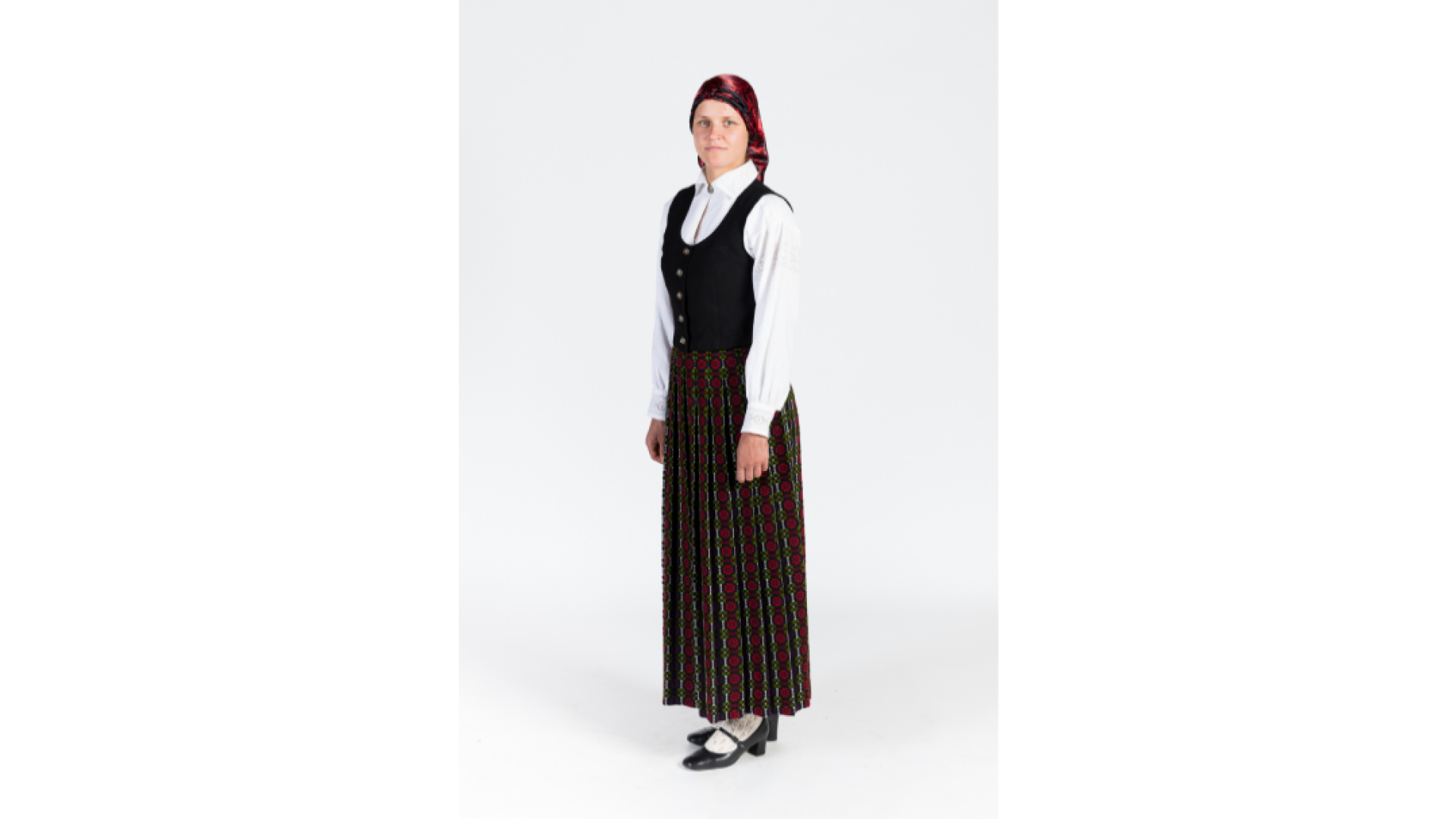 Jauna sieviete Zemgales tērpā. Tumši rozīšu brunči, tumša auduma ņieburs, krekls, galvā zida lakats, baltas, adītas zeķes, kurpes. 