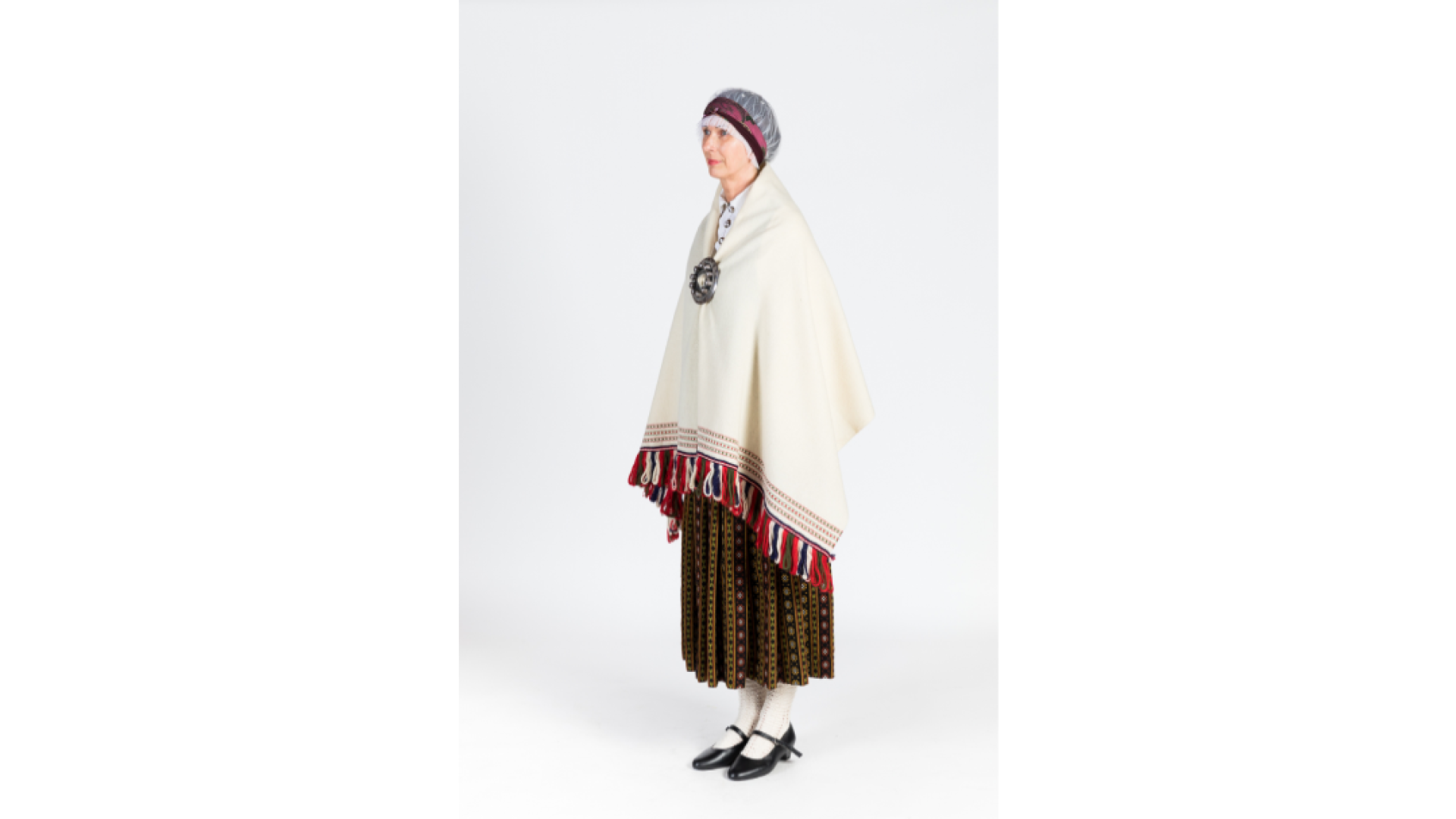 Sieva Zemgales tērpā no sāniem. Balts, krekls, rozīšu burunči, zaļa auduma ņieburs, balta villaine, kas sasprausta ar lielo saktu, galvā tilla aube, kas pārsieta ar lakatiņu, kājās baltas zeķes un melnas kurpes.